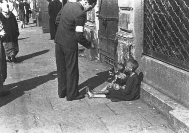 A Warsaw ghetto resident gives money to two children on a Warsaw ghetto street